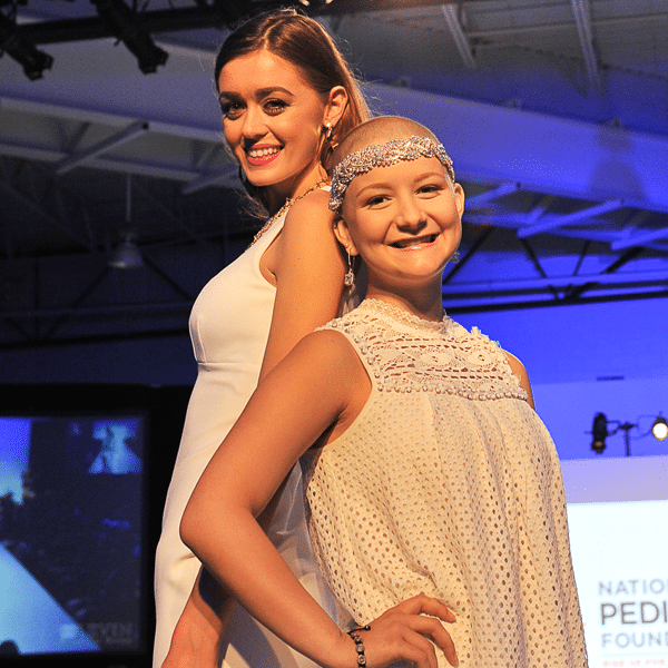 A female fashion model posing next to a young female cancer survivor at a runway event