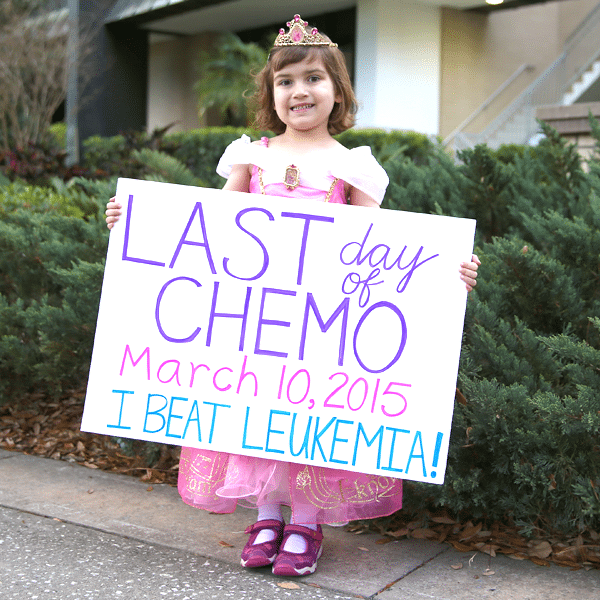 Little girl in princess outfit holding a sign saying last day of chemo and that she beat Leukemia