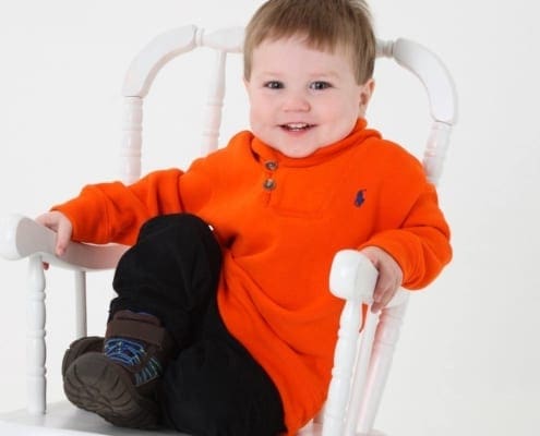 Portrait of Jonathan in a white rocking chair and orange sweater smiling